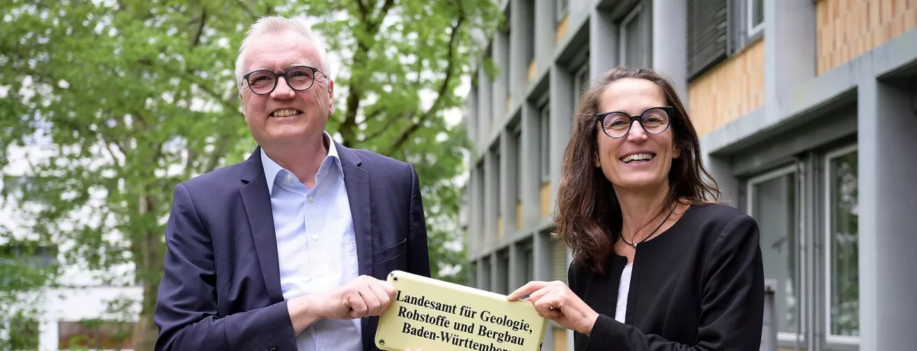 links ein weißhaariger, lächelnder Herr mit Brille - rechts eine dunkelhaarige, lächelnde Frau mit Brille; beide halten gemeinsam ein Schild des LGRB