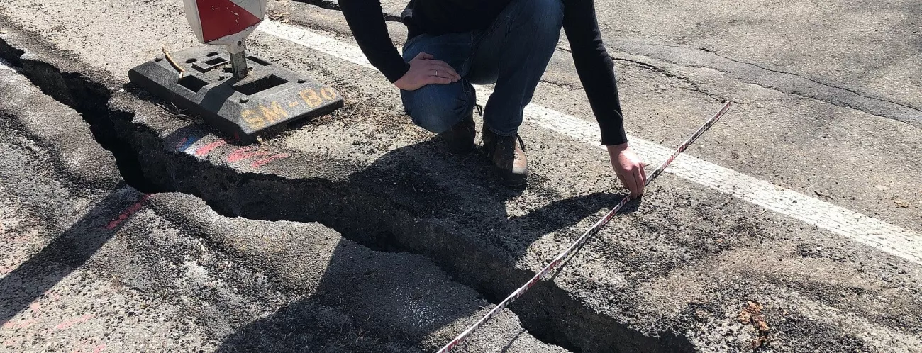 Ein Mann kniet an einem Längsriss einer Straße und misst mit einem Meterstab dessen Breite