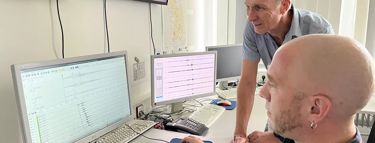 Zwei Männer betrachten Seismogramme auf zwei Bildschirmen