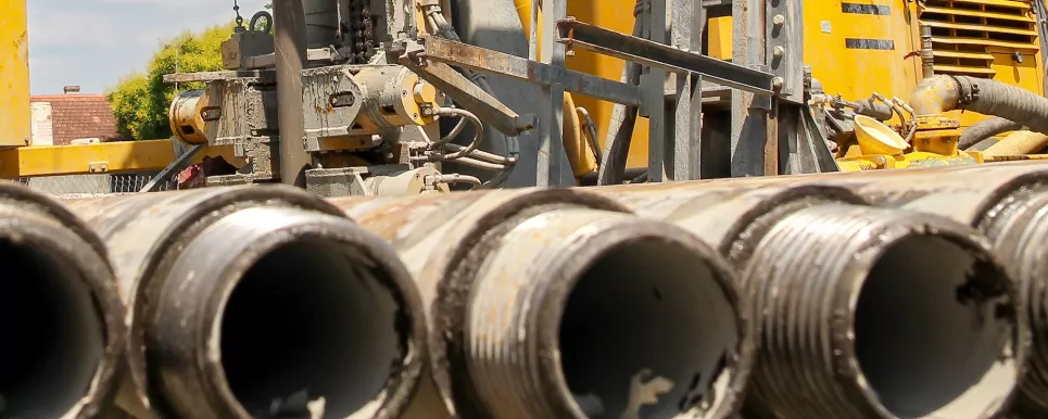 Foto zeigt im Vordergrund Metallrohre, im Hintergrund ein gelbes Bohrgerät